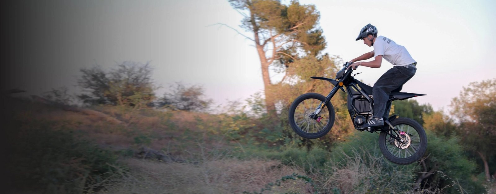 Rider jumping Freego Nova5 electric dirt bike over dry woodland hills at dusk
